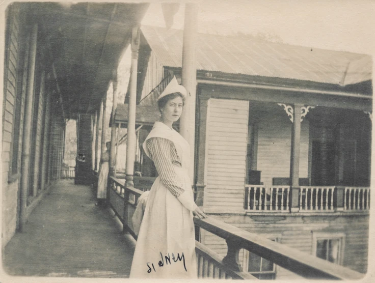 an old po shows a woman in dress standing on porch next to a house