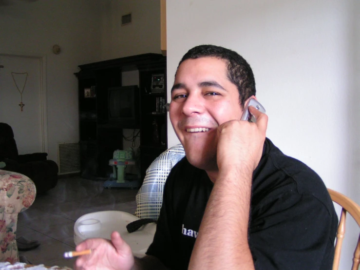 man sitting on chair with cellphone to his ear as he smiles