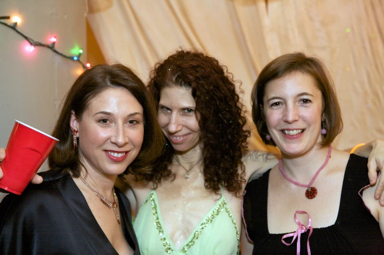 three women pose for the camera holding cups