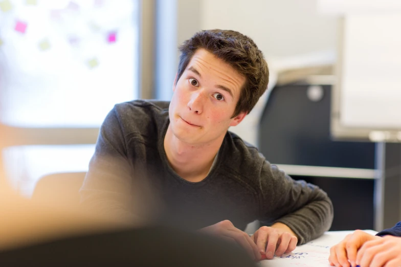 a young man sitting at a table looking into the camera