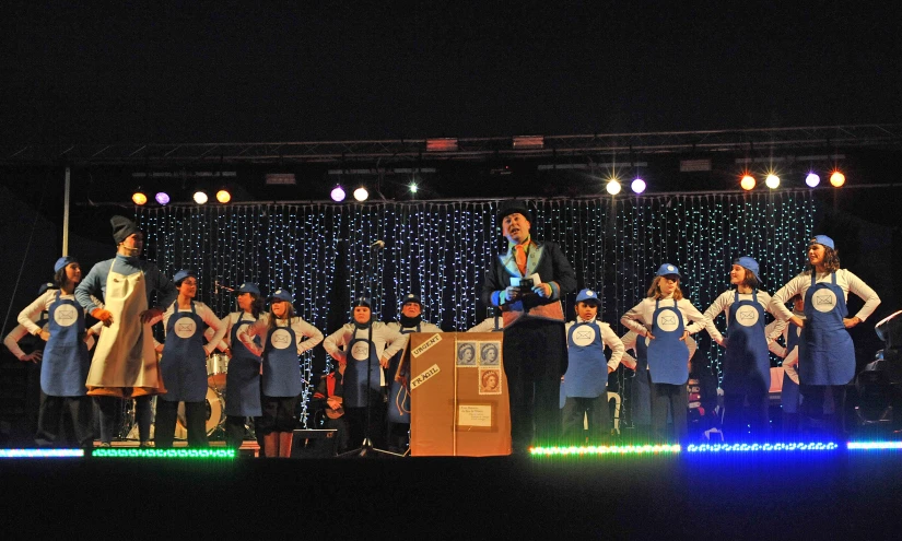 performers are dressed in aprons while an audience looks on