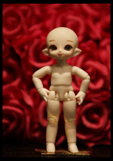 a small white doll with a brown head standing next to some red roses
