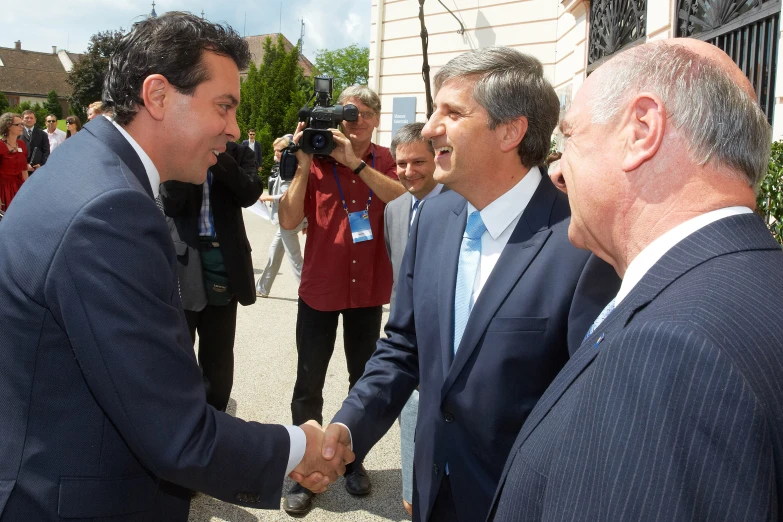 three men shake hands as people watch and take pictures