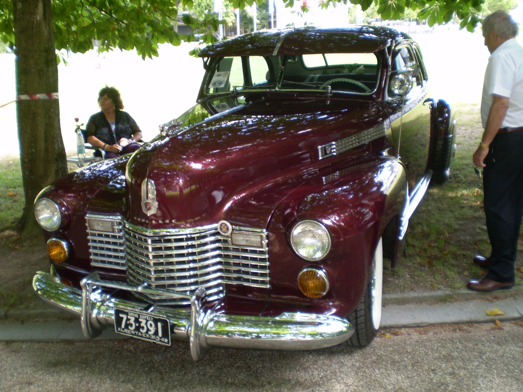 a vintage maroon sedan parked by some people