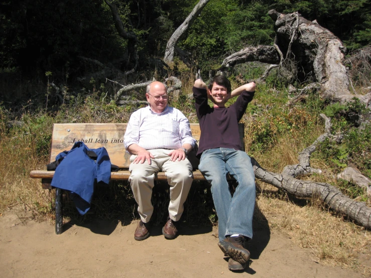 two men sitting on a wooden bench with their arms up