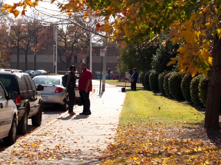 two men standing by a sidewalk near many parked cars