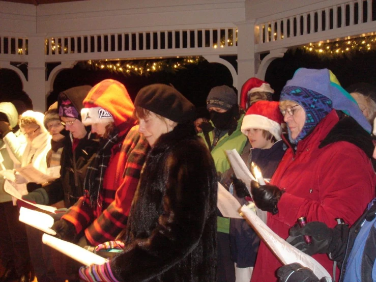 several people in winter hats standing around a campfire