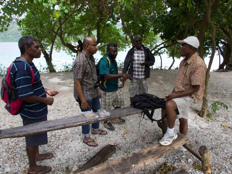 men are gathered around on a bench on the beach