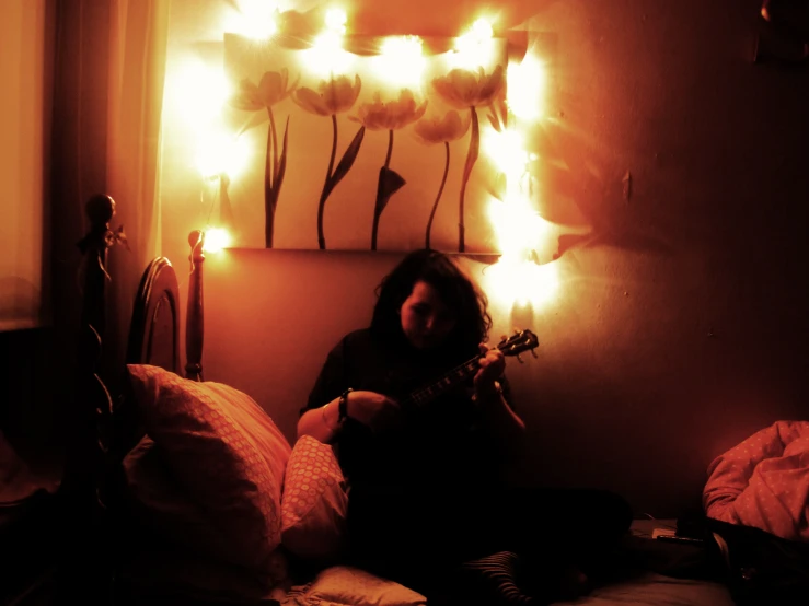 the  is sitting on her bed playing an acoustic guitar