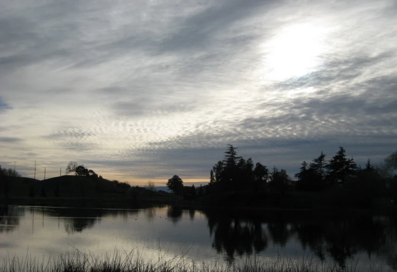 a lake in the sunset with some clouds over it