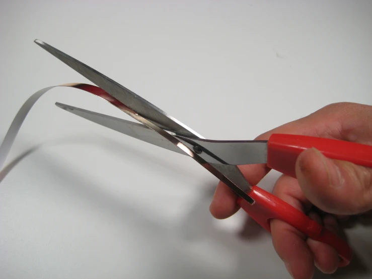 hand  red handled scissors on white surface