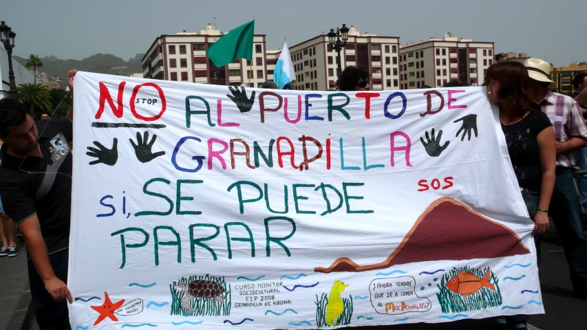 a protest banner in spanish with a group of people walking near by