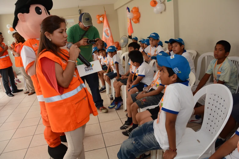 s wearing safety gear and orange vests standing around and looking at a man talking to them