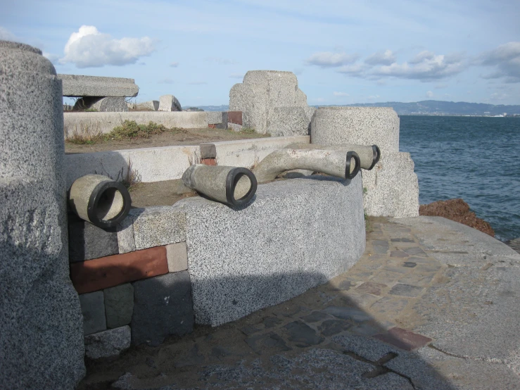 some gray stones and black objects on a wall by the water