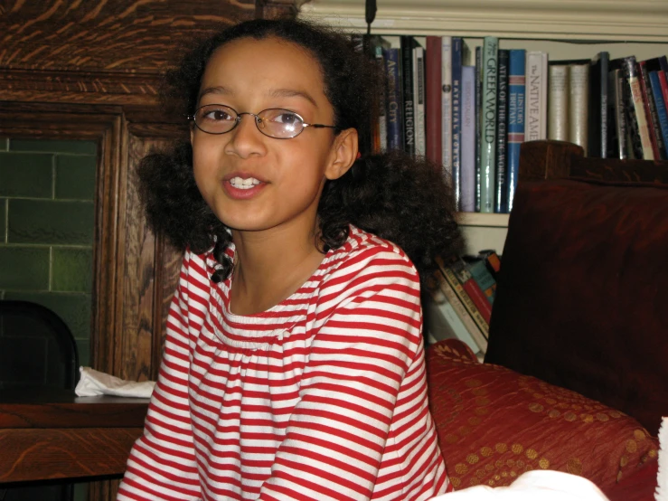 a girl wearing glasses posing in front of a bookcase