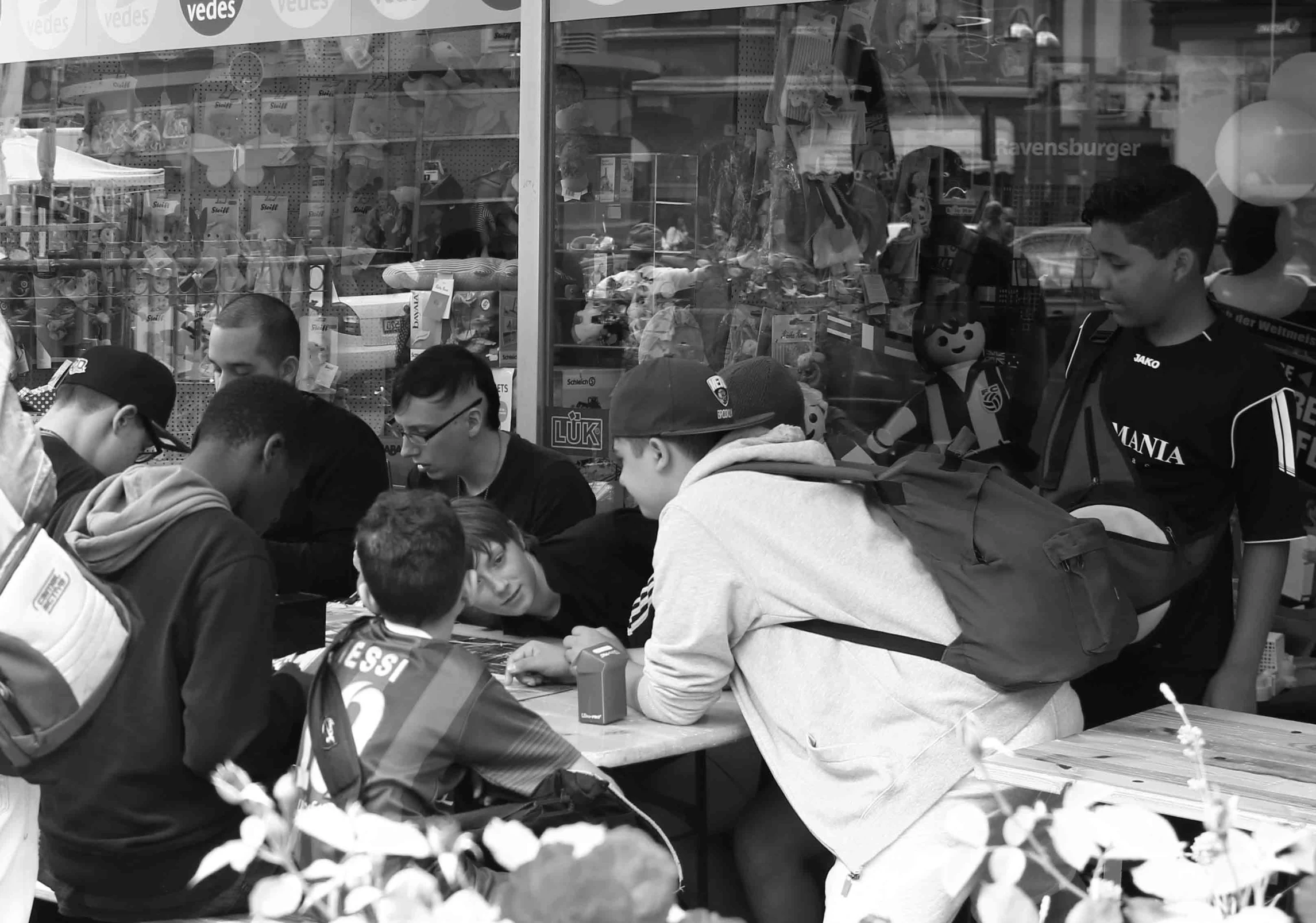 people at tables in front of a store on the side of a street