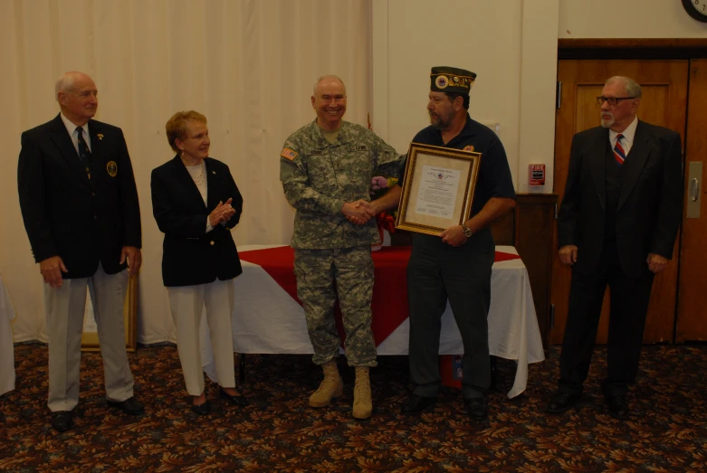 an old soldier holding up a certificate to another man in uniform