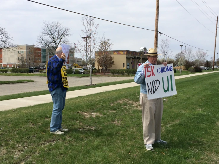 two men are standing on the sidewalk and one is holding a sign