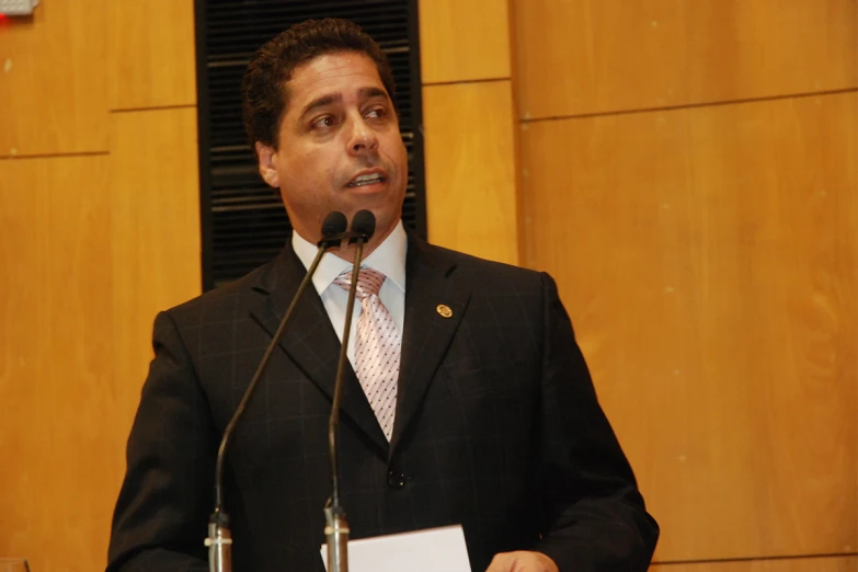 a man speaking at a podium with microphones in front of him