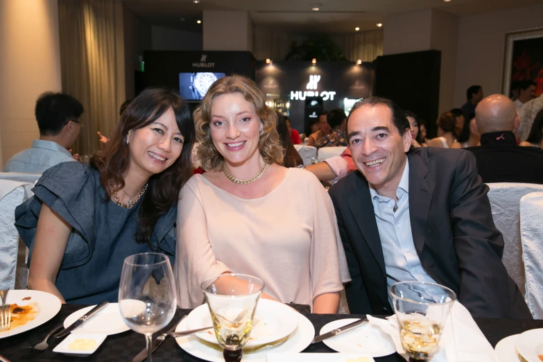 three people sitting at a table in front of white plates with food