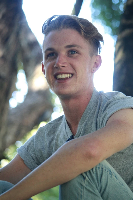 a young man smiles for a po while sitting underneath a tree