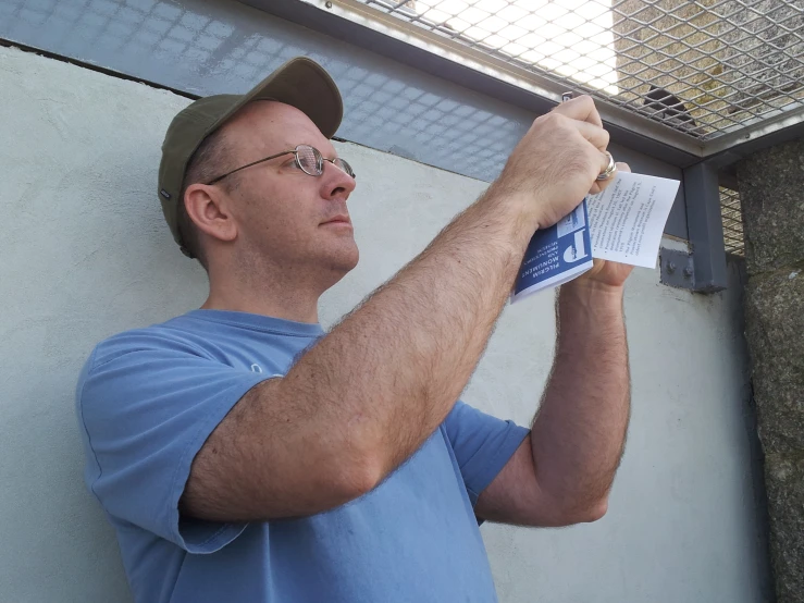 a man leaning against a wall holding up a book