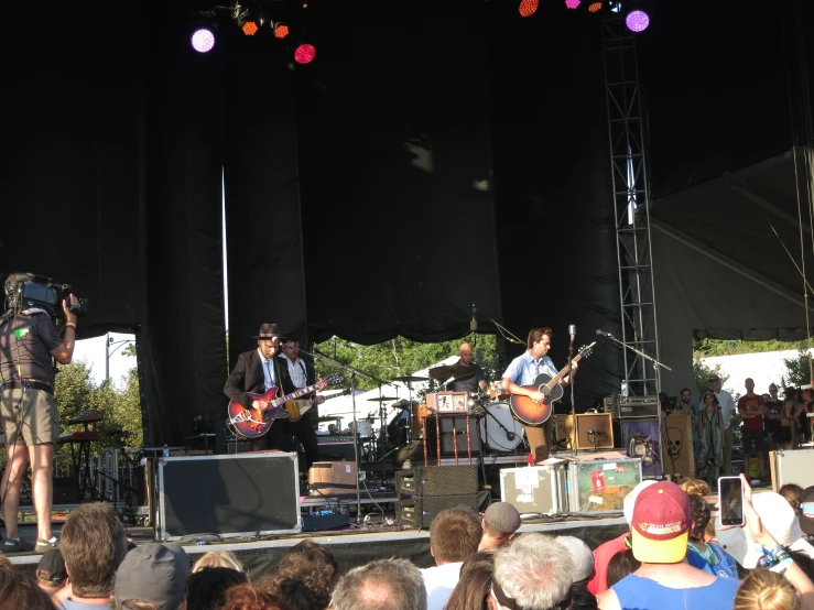 group of men on stage playing guitar and singing to large crowd