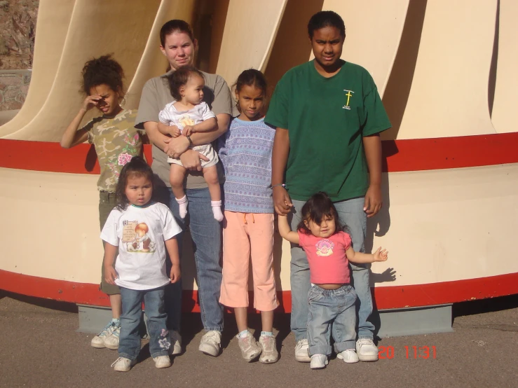 two adults, one , and seven children are standing next to a sculpture