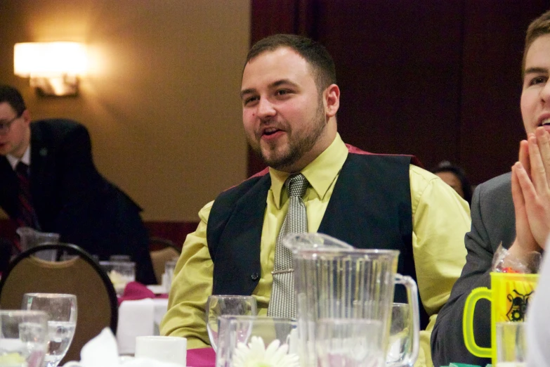 two men sitting at a table talking and clapping