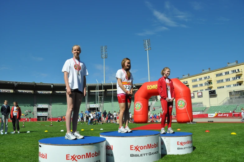 two girls standing on top of a race podium in front of some people