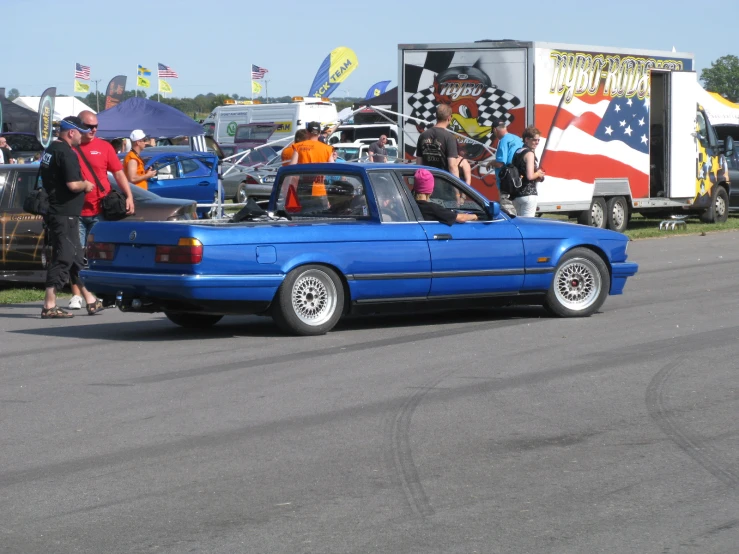 a blue car is parked by a truck with people standing around