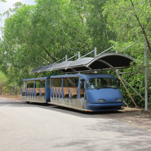 a blue and white train parked under a canopy on the side of the road