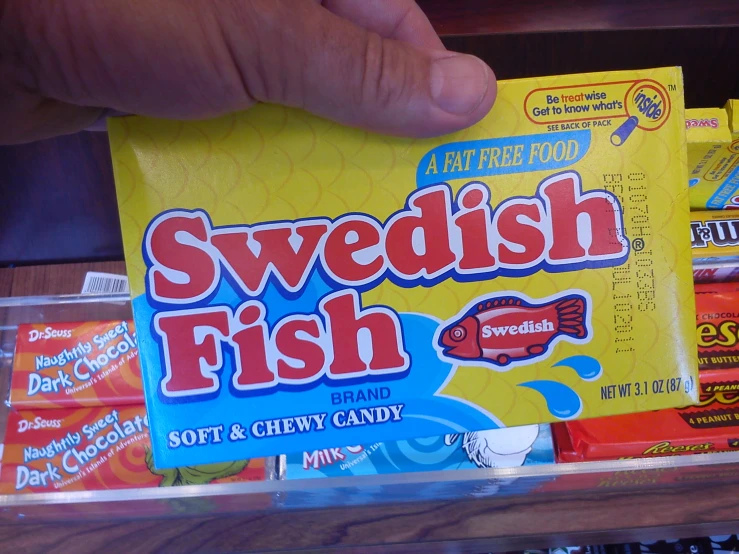 someone holds up swedish fish next to some candy