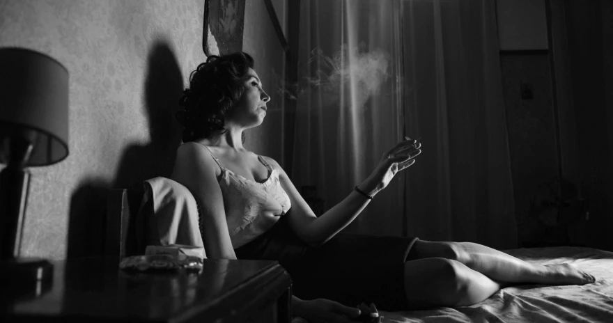 woman smoking cigarette sitting on a bed with a window