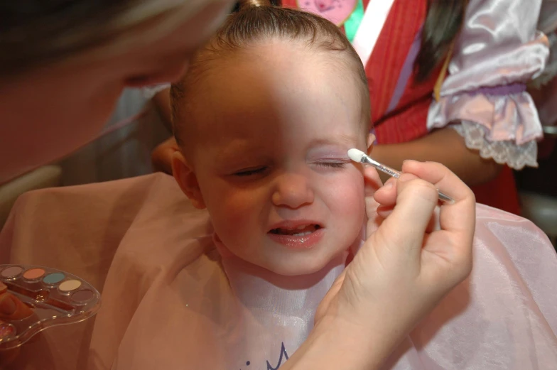 a young child gets make - up done by an adult