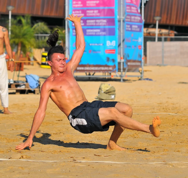 shirtless male volleyball player stretches for a ball on sandy beach