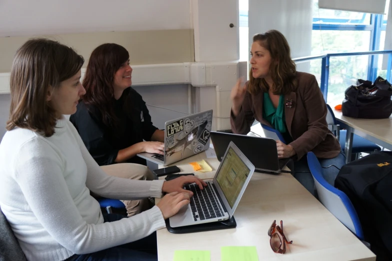 two women sit with laptops at a table