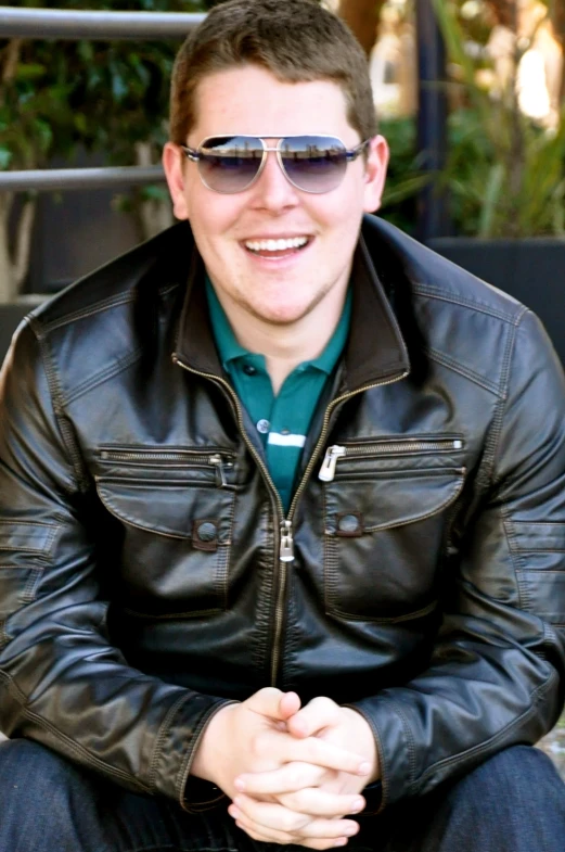the man is smiling wearing a black leather jacket and blue shirt