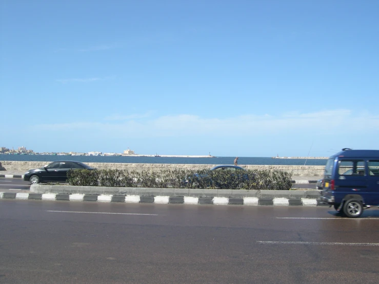 a blue bus is driving on the road near the ocean