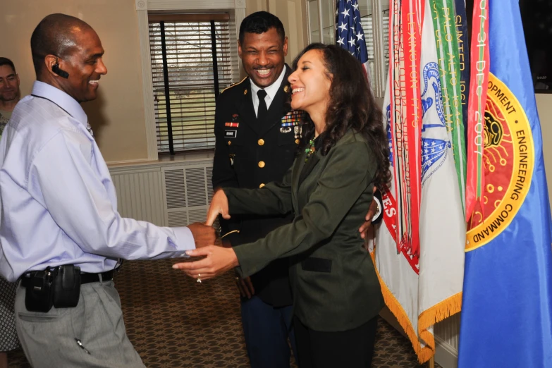 two smiling army officers shake hands while others look on