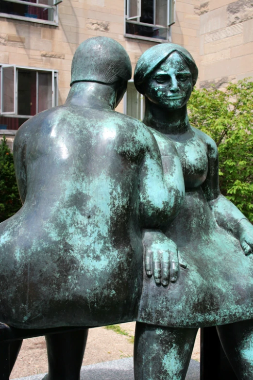 a green sculpture of two people, with one holding the other, in front of a tall building