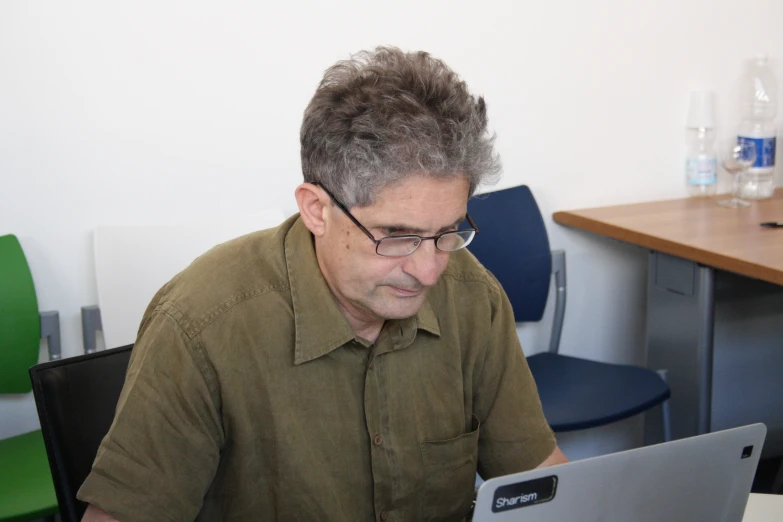 a man in glasses sits at a table working on a laptop