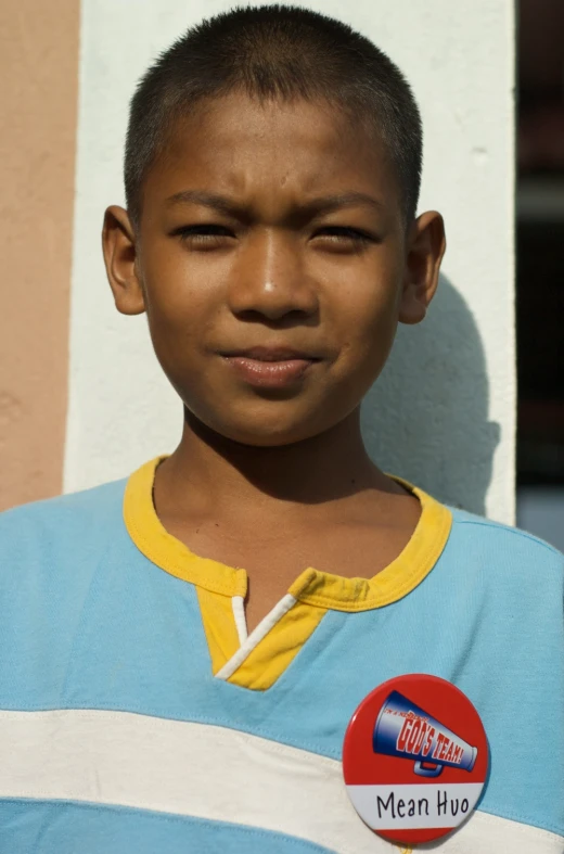 a boy standing against a building and wearing a badge