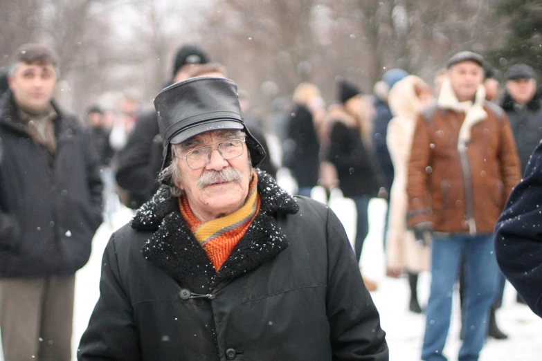 old man with moustache in snow near large group of people
