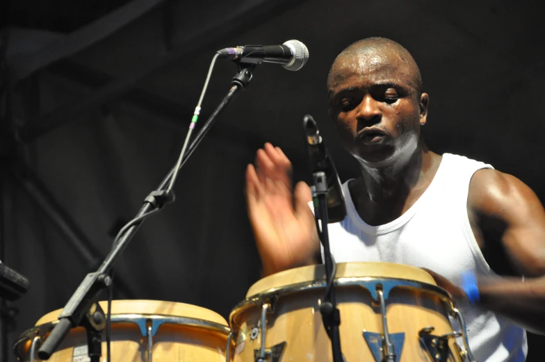 a man stands next to two drums and sings