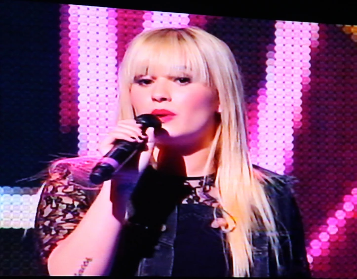 a blonde girl on a stage singing into a microphone