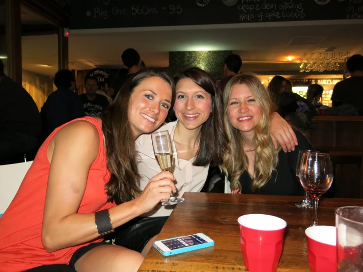 three women are posing with their wine glasses at a restaurant