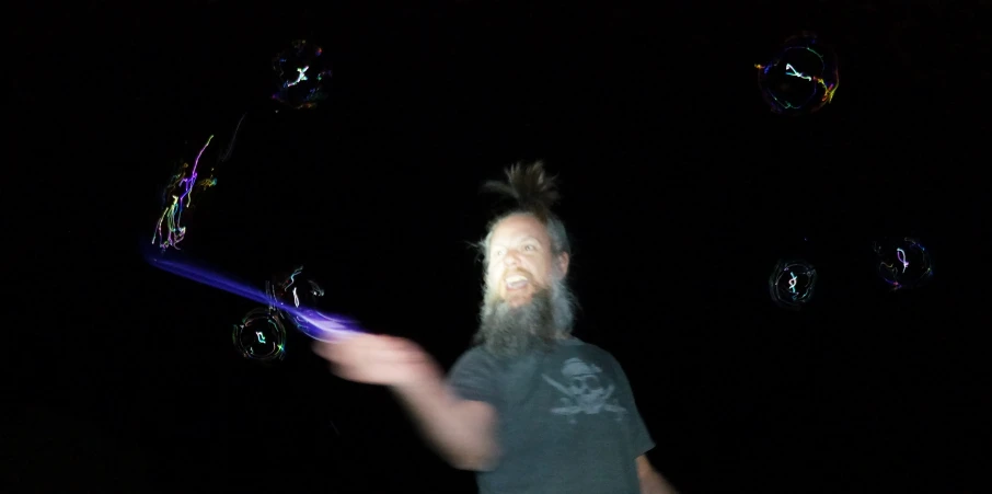 a man with long hair is flying bubbles in the dark