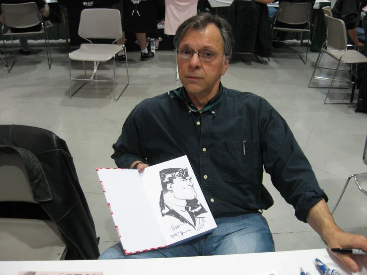 a man in glasses holding a sketch in front of him