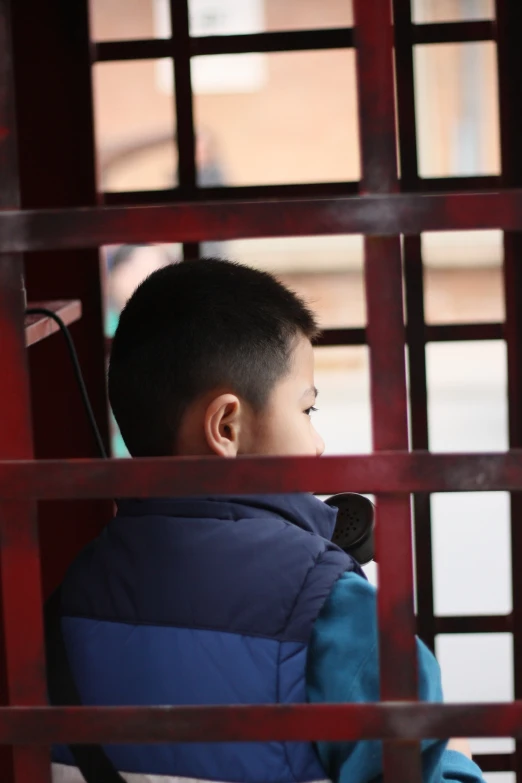 a young child with black hair is looking out through an outdoor window